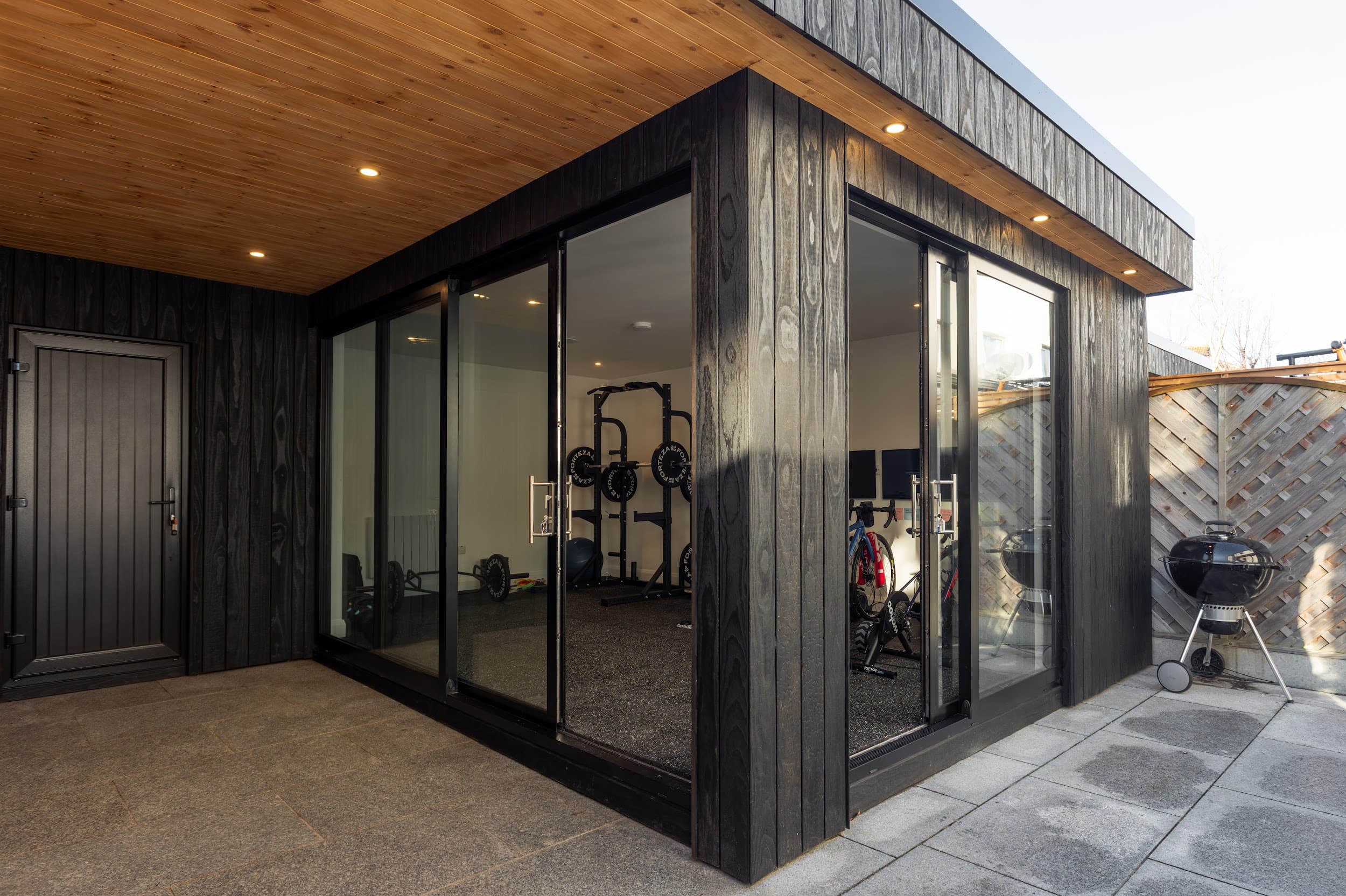 Modern garden gym interior with weights, mirrored wall and warm timber finish